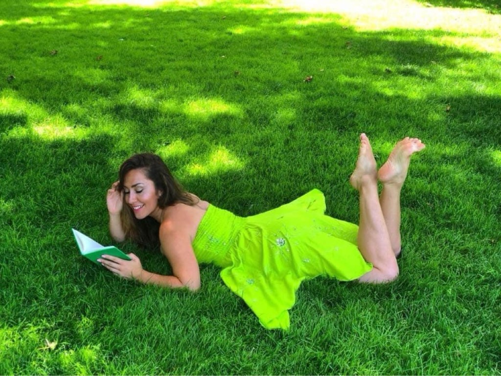 CarOlé Flamenco reclining on bright green grass in a flowing grass-green dress, reading a book