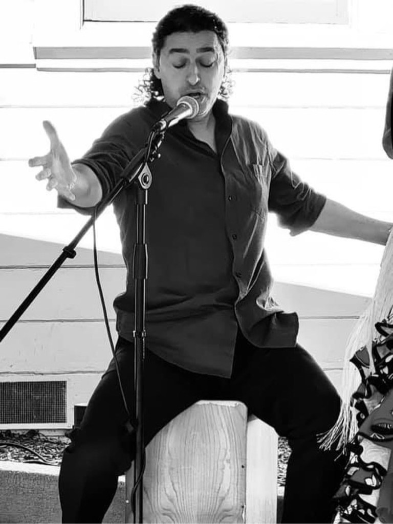 Azriel 'El Moreno', cantaor, singing into a microphone seated on a cajón