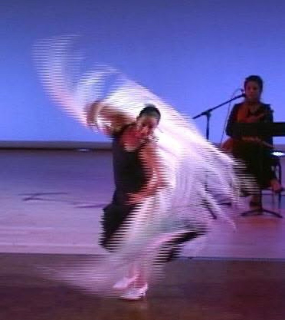 CarOlé Flamenco spinning with a white mantón on a blue-lit stage