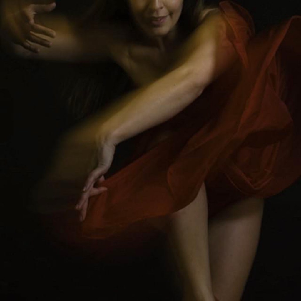 CarOlé dancing in flowing red fabric against a black background